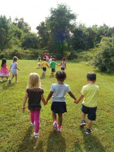 Children holding hands while others play outside. 