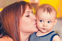 Mom affectionately kissing her wide-eyed baby on the cheek