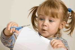 Little girl in pigtails concentrates on cutting a piece of paper with scissors