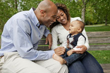 Father and mother with adored baby on lap, on a park bench