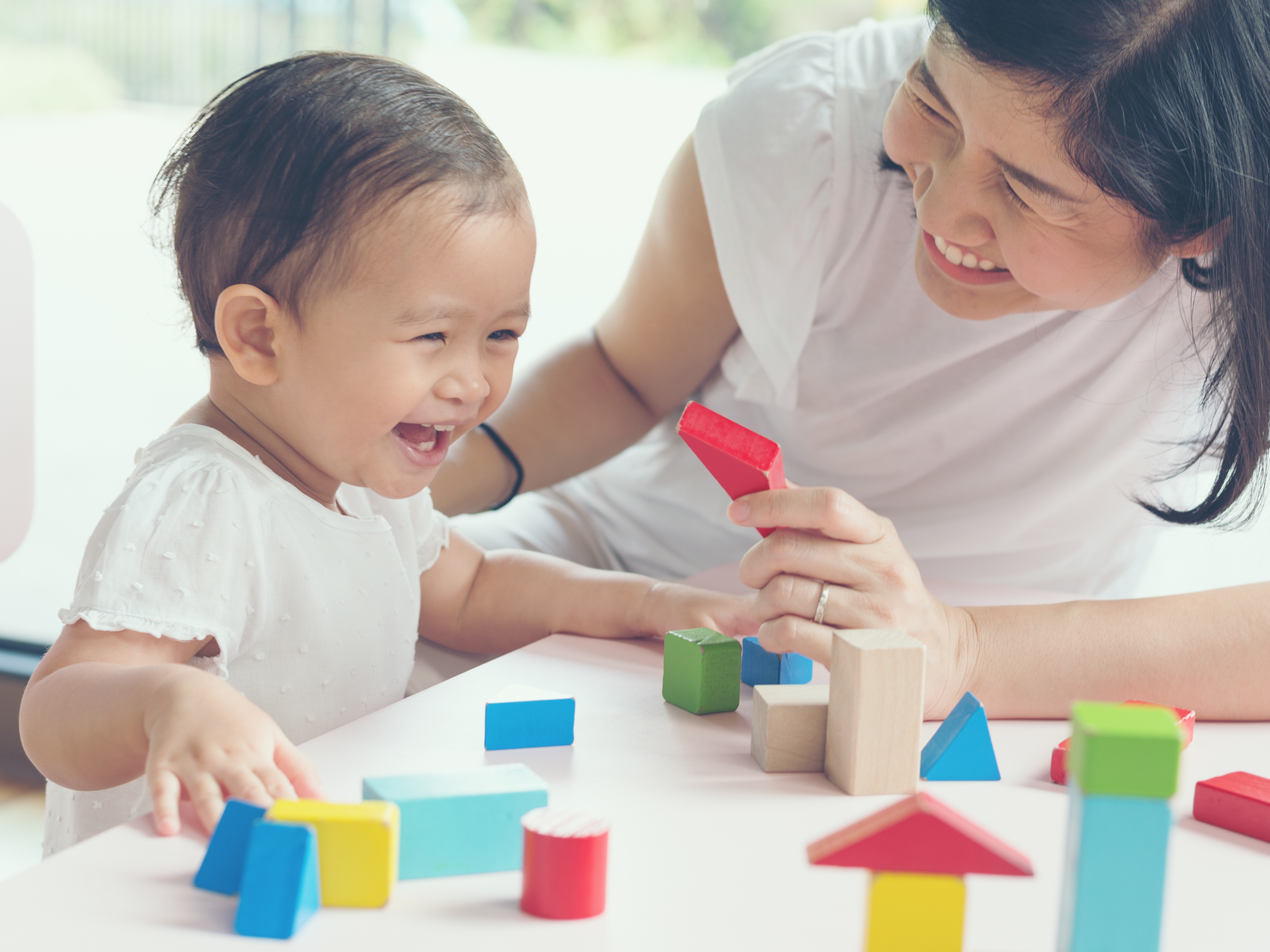 Asian mom and young daughter smiling playing with blocks