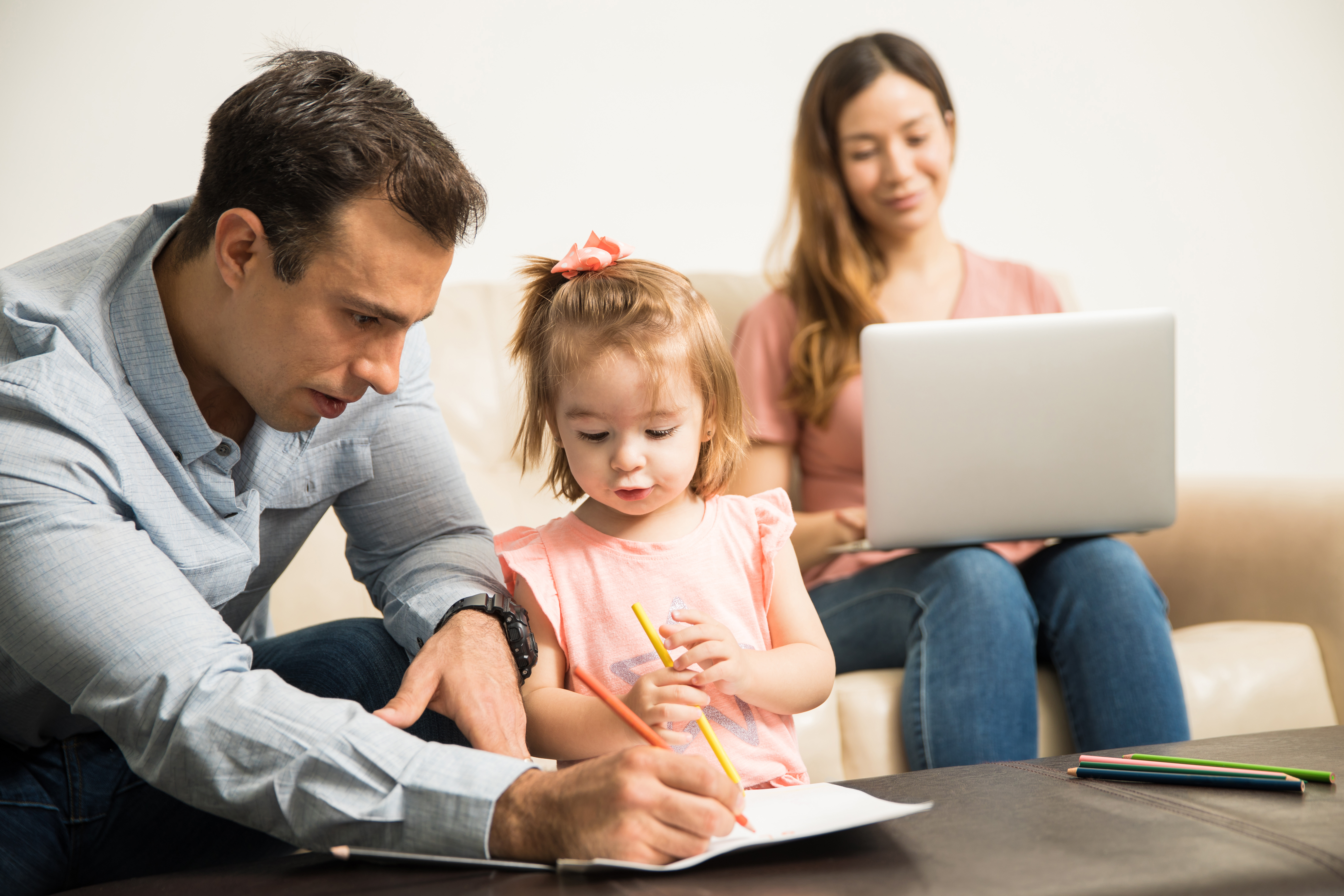 Latin dad drawing with her attentive daughter while her happy mom works in her laptop