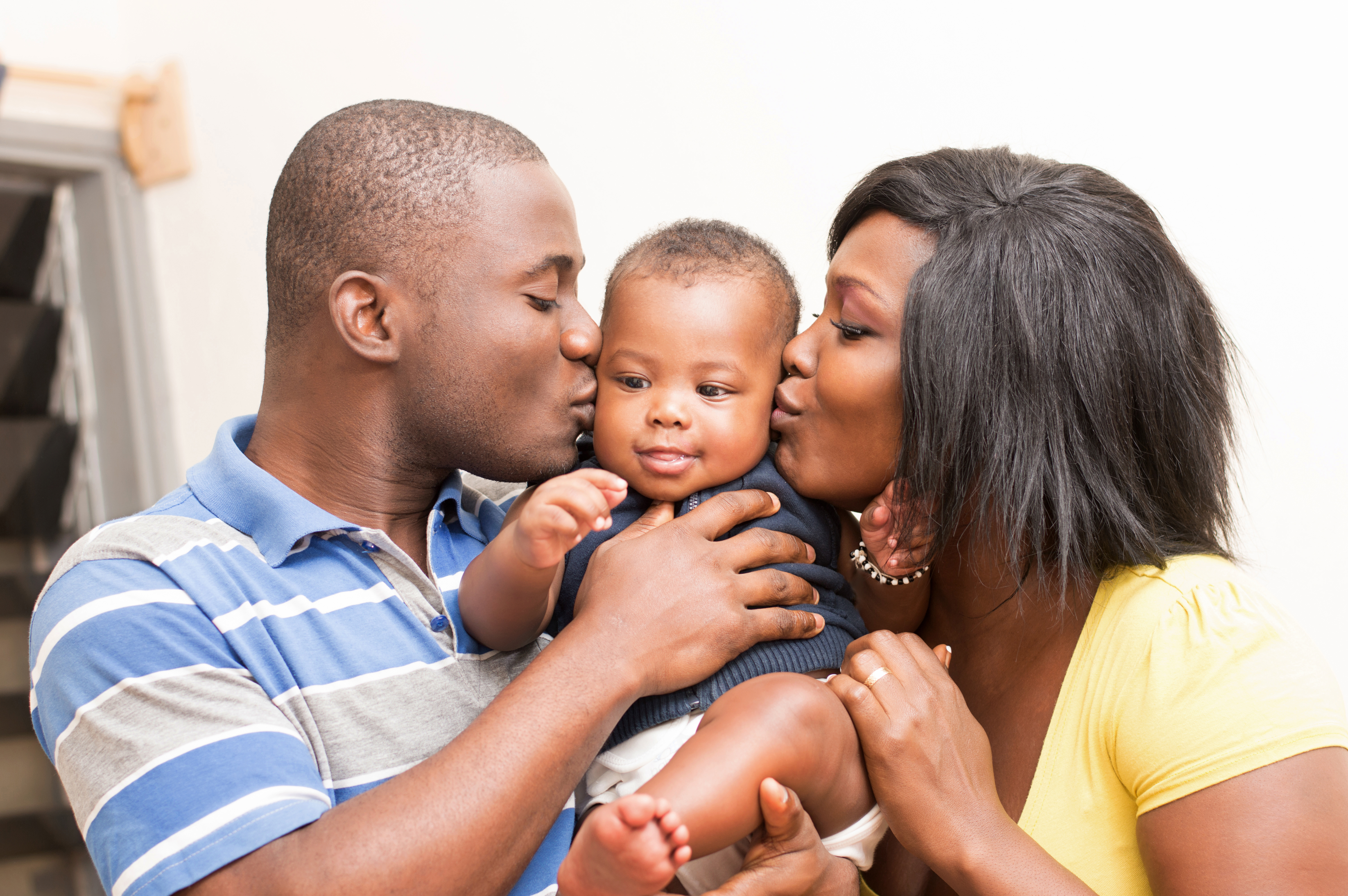 African American parents holding and kissing their infant son on his cheeks
