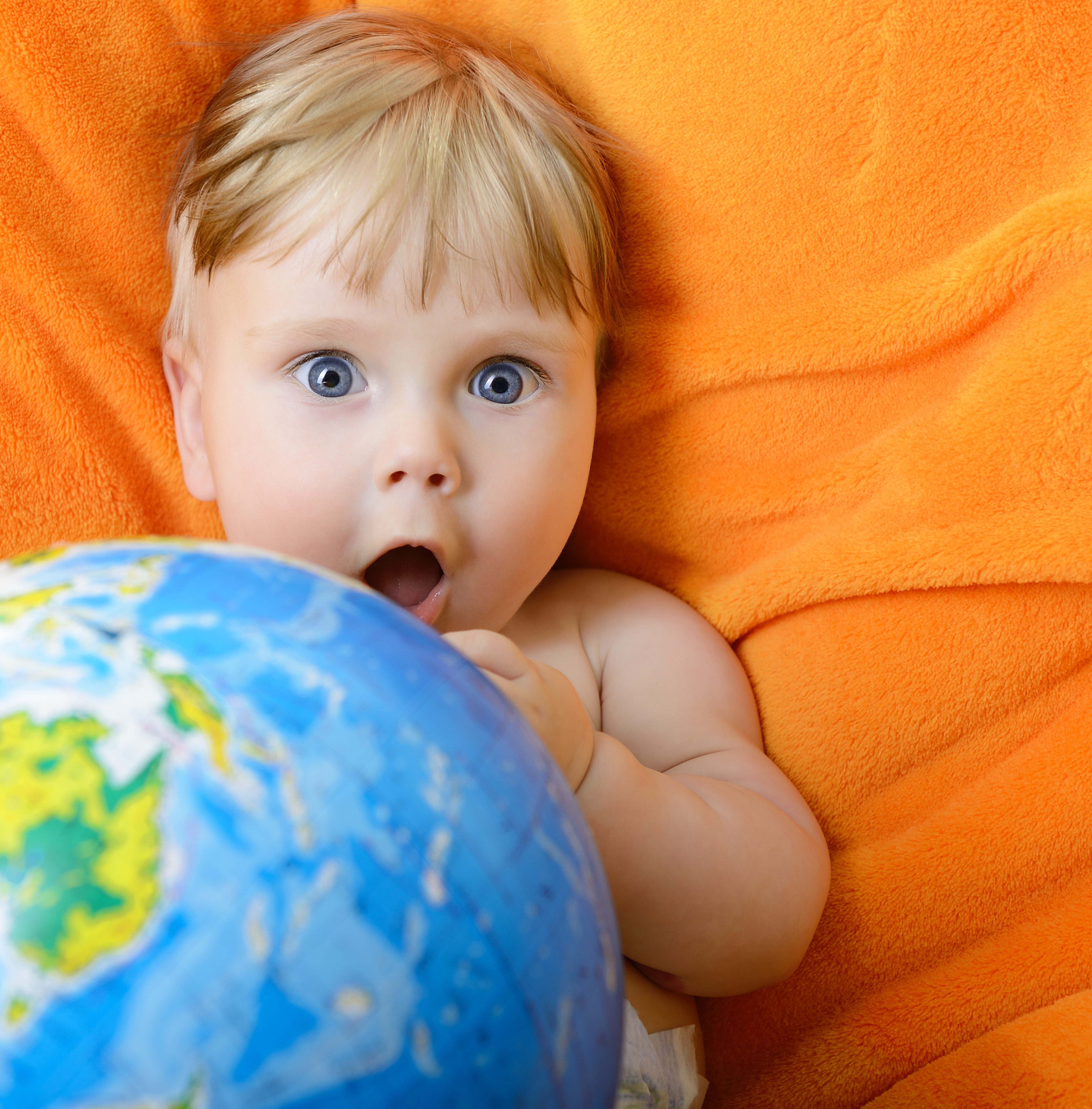 Happy baby playing with terrestrial globe on an orange plaid